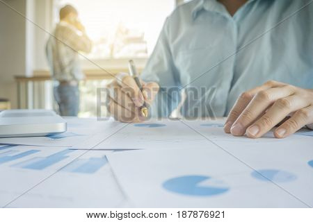 Handsome young businessman working with laptop while sitting on the desk in office and financial statistic graph.