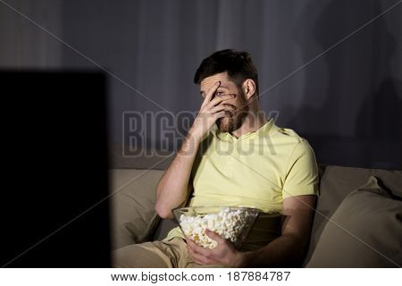 people, mass media, television and entertainment concept - scared young man watching tv and eating popcorn at night at home