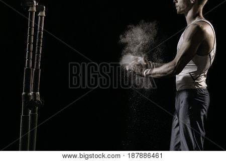 Male athlete rubs hands with talcum powder in front of gymnastic parallel bars