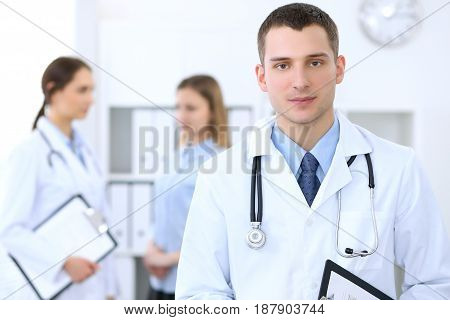 Friendly male doctor  on the background with patient  and physician in hospital. High level and quality medical service concept.