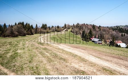 mountain meadow with hiking trail few houses forest and clear sky bellow Jakubovsky vrch in Javorniky mountains in Kysuce region of Slovakia during nice spring day