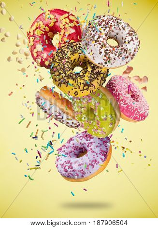 Tasty donuts in motion falling on pastel yellow background, close-up.