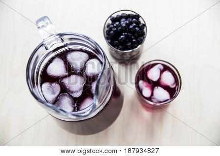 Blueberry juice in a decanter and a glass next to frozen berries