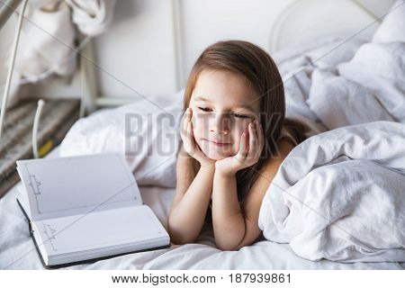 Portrait of a little girl in the bed reading a book. Activities, hobbies