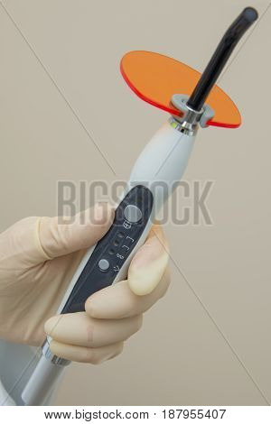 Hand in medical glove holding Dental UV curing light. Ultraviolet polymerization Lamp with orange blocking glass.