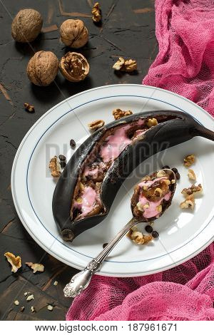 Bananas baked in peel on grill with chocolate drops and marshmallow. Black peel serves as natural pot for delicious banana dessert. Dessert is served hot sprinkled with walnuts. Eat with spoon