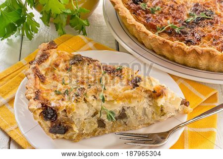 Delicious homemade quiche with cabbage and dried prunes. Vegetarian pie. Large pie and slice on plates supplemented with fresh parsley and thyme yellow napkin white wooden table