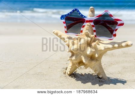 Patriotic USA background with starfish in the sunglasses on the sandy beach