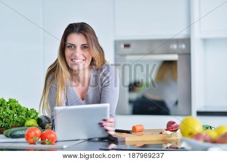Young woman is making online shopping by tablet computer. Housewife found new recipe for cooking in a kitchen.