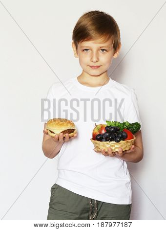 A blond boy chooses between a burger and fresh vegetables and fruits.