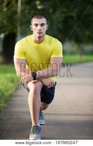 Fitness man stretching arm shoulder before outdoor workout. Sporty male athlete in an urban park warming up
