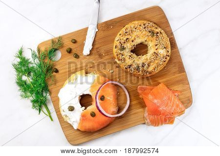 Bagel ingredients. Lox, purple onions, capers, dill, and the buns, shot from above on a wooden board and a white marble background in the process of making, with a place for text