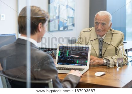 Young financial advisor sitting in front of laptop, consulting senior client with his investment strategy.
