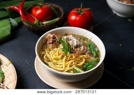 Asian soup noodles and chicken in bowl on dark background. 