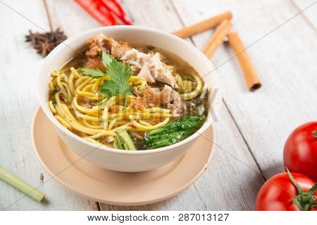 Asian soup noodles and chicken in bowl on wooden background. 