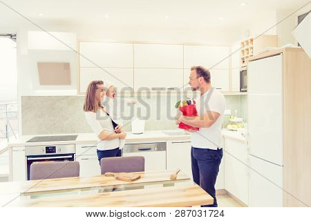 Happy Parents Standing In The Kitchen And Prepares For Cooking With Their Baby Girl Chef. Father Bri