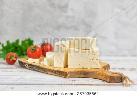 Large Pieces Of Feta Cheese On Old Wooden Cutting Board And Cherry Tomatoes On Light Background. Sel