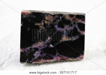 Natural Mineral Stone - Polished Charoite Gemstone On White Cement Background.