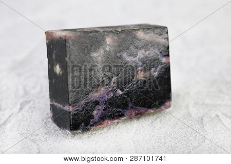Natural Mineral Stone - Polished Charoite Gemstone On White Cement Background.