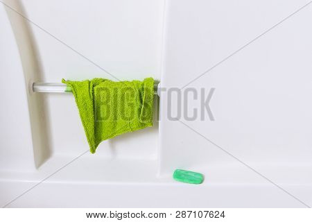 Horizontal Close-up Shot Of The Wall Of A White Bathtub.  Green Washcloth Hanging From Handrail And 