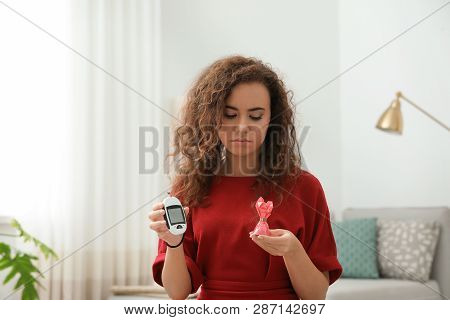 Upset African-american Woman Holding Digital Glucometer And Candy At Home. Diabetes Diet