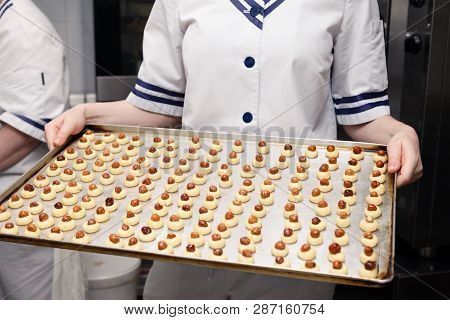 Сloseup Of Pastry Chef In Uniform At Restaurant Professional Kitchen Holding Baking Tray With Small