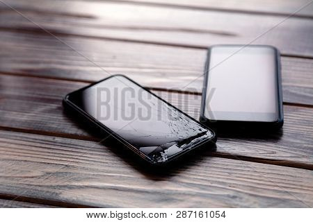 Сloseup Black Smartphone With Broken Screen Glass Lying On Wooden Table. Concept Of Dropping Phone,
