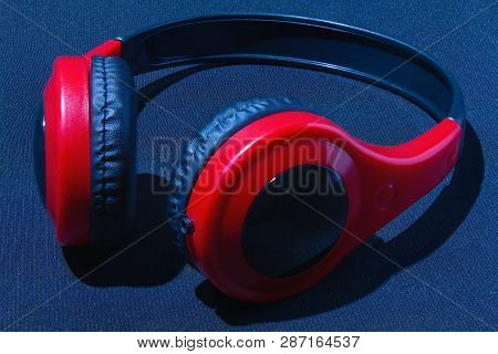 Red Headphones On A Dark Background. Audio Headphones On The Table. Dark Red Headphones Background.