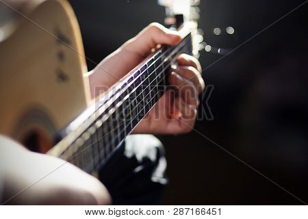 A Man Plays A Song On An Acoustic Wooden Guitar, Brightly Lit By Sunlight