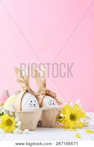 Easter Colored Eggs With Painted Faces In Paper Tray With Decorationd On Pink Background