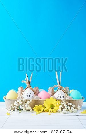Easter Colored Eggs In Paper Tray With Decorationd On Blue Background