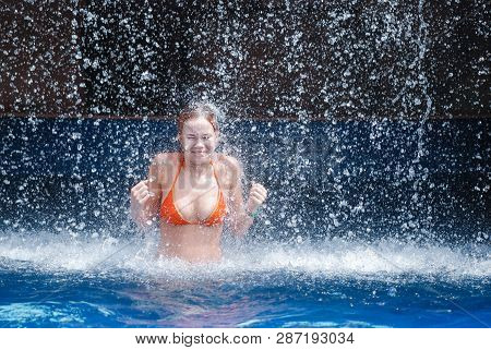 Laughing And Happy Girl In An Orange Swimsuit Plays Jumping And Having Fun Under A Waterfall In The 
