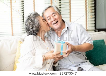 Happy Asian Senior Couple Having Anniversary Day, Bearded Husband Presenting A Packing Gift And Wife