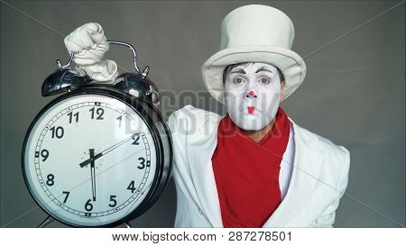 Mime In A Suit And Hat Is Holding A Big Clock. Man In A Suit With A Dial In His Hands. Actor With A 