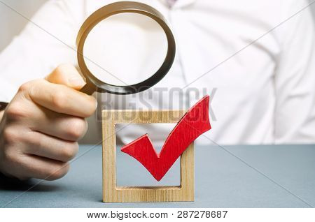 A Man Examines A Red Check Mark Through A Magnifying Glass. Assessing The Transparency Of The Legiti