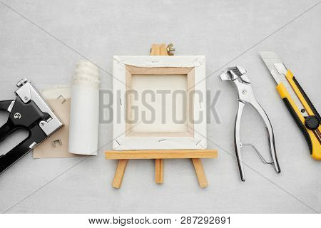 Artist Canvas On Wooden Easel, Canvas In Roll, Canvas Stretcher Pilers, Knife And Staple Gun On Marb