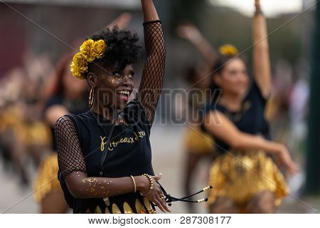 New Orleans, Louisiana, USA - February 23, 2019: Mardi Gras Parade, African American dancer from Ritmeaux Krewe, wearing yellow flowers on her head, smiling and dancing