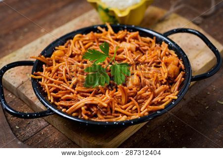 closeup of a spanish fideua, a typical noodles casserole with seafood, in a paella pan and aioli sauce in a yellow mortar on a rustic wooden table
