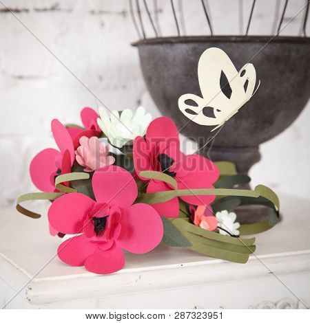 Closeup Of Paper Flowers On A Starov Desk With A Metal Cage And A Brick Wall In The Background.