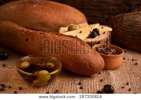 Fresh Bread Baguette With Olive Oil, Olives. Cheese And Rosemary On Wooden Background. Teasty Breakf