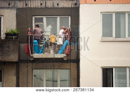 Two Workers Are Plastering The Facade Of A Building Without Observing Safety Techniques In A Cradle 