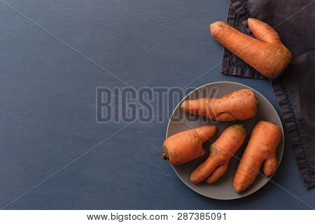 Misshapen Ugly Fresh Carrots With Imperfections And Splits On A Plate Viewed From Overhead On Grey W
