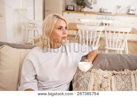 Indoor Portrait Of Beautiful Pensive Middle Aged Woman In Her Forties Relaxing In Stylish Cozy Home 