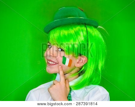 Child Celebrating St. Patricks Day Showing His Make-up. A Small, Curly Boy In Green Carnival Accesso