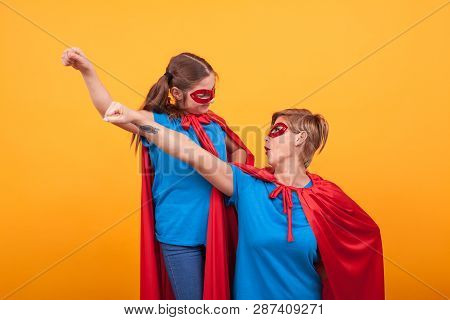 Mother And Daughter Looking At Each Ohter With Their Fist In The Air Dressed Like Heroins.