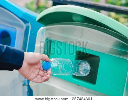Closeup Of Man Hand Throwing Empty Plastic Water Bottle In Recycling Bin.