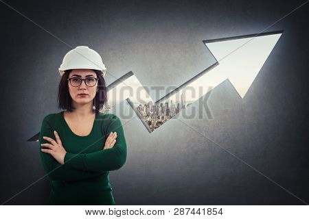 Woman Engineer, Wearing Protective Helmet, Holding Arms Crossed, Thoughtful Looking Over A Rising Gr