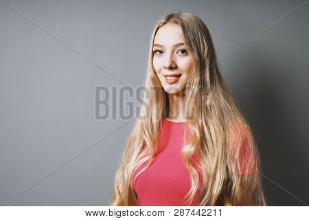 Happy Smiling Young Woman With Long Blond Hair And Pink T-shirt Against Gray Background With Copy Sp