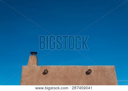 Exterior Red Adobe Framed By Blue Sky, Chimney And Exposed Beams, Copy Space, Horizontal Aspect