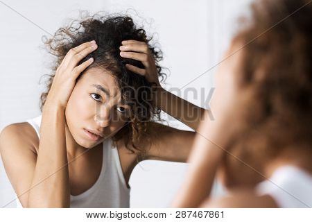 Afro-american Girl Frowning And Looking Intently On Her Face In Mirror. Hair And Sculp Problems Conc
